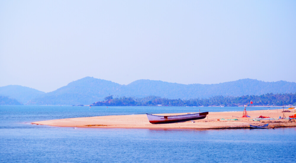 Lonely fisherman boat on the coast near Palolem beach. Talpona river. Mountain on the background.